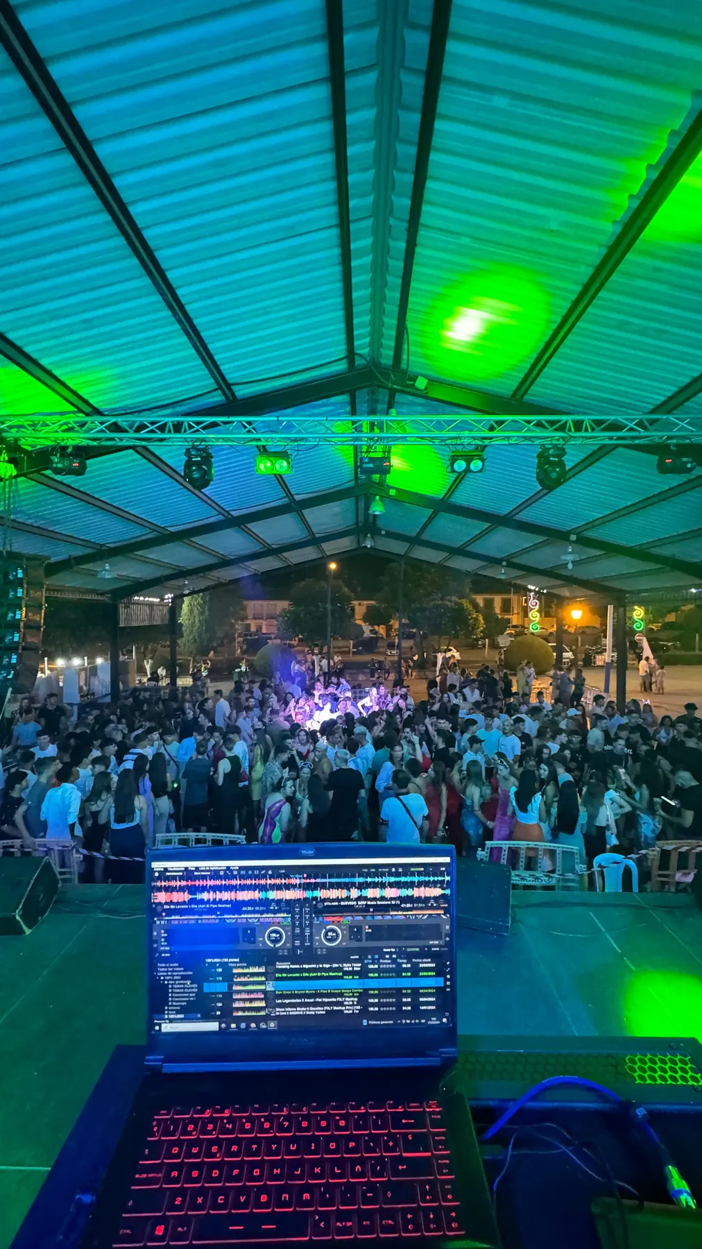 Vista desde la cabina del DJ de una caseta llena de gente con iluminación verde